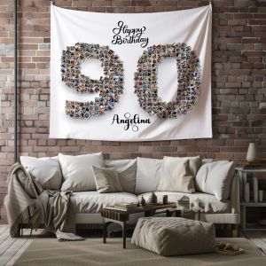 a cozy living room with a white couch adorned with beige and taupe throw pillows. A beige blanket is draped over the left arm of the couch, and a tufted ottoman sits in front. The room has a rustic feel with exposed brick walls and a wooden floor. Hanging on the wall behind the couch is a large, white tapestry. The tapestry displays the number "90" in a collage style, created from numerous small photos, and is personalized with the name "Angelina." Above the number, the text reads "Happy Birthday" in elegant script. The overall ambiance of the room is warm and inviting, with a blend of modern and rustic elements.